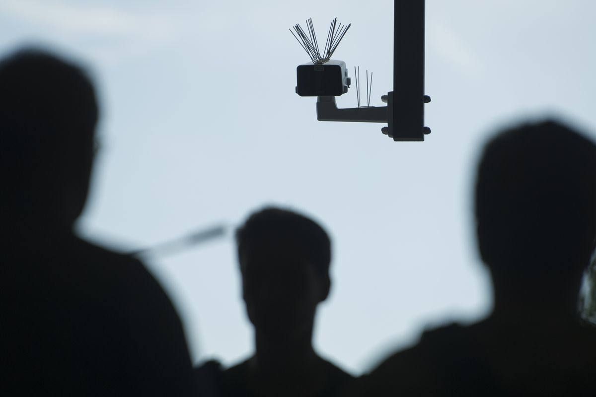 Surveillance camera with silhouetted people near it.