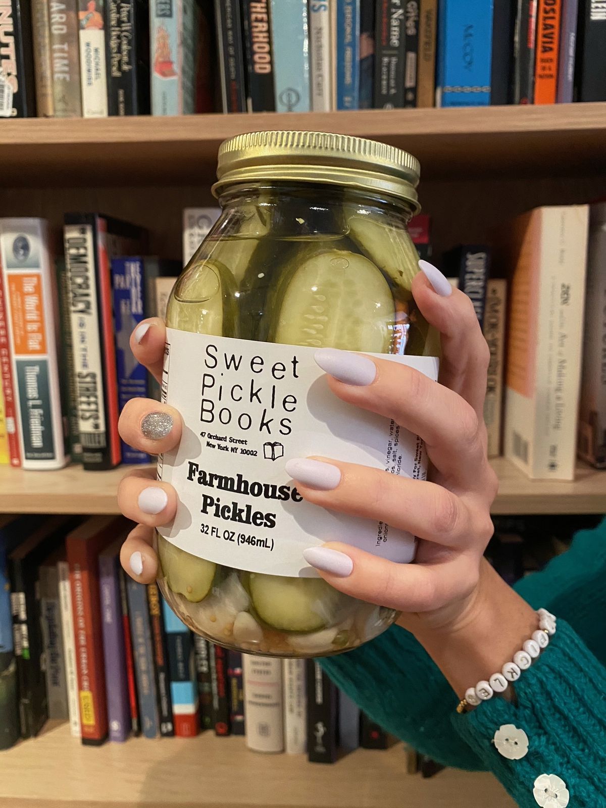 Two hands gripping a pickle jar with a bookshelf full of books in the background