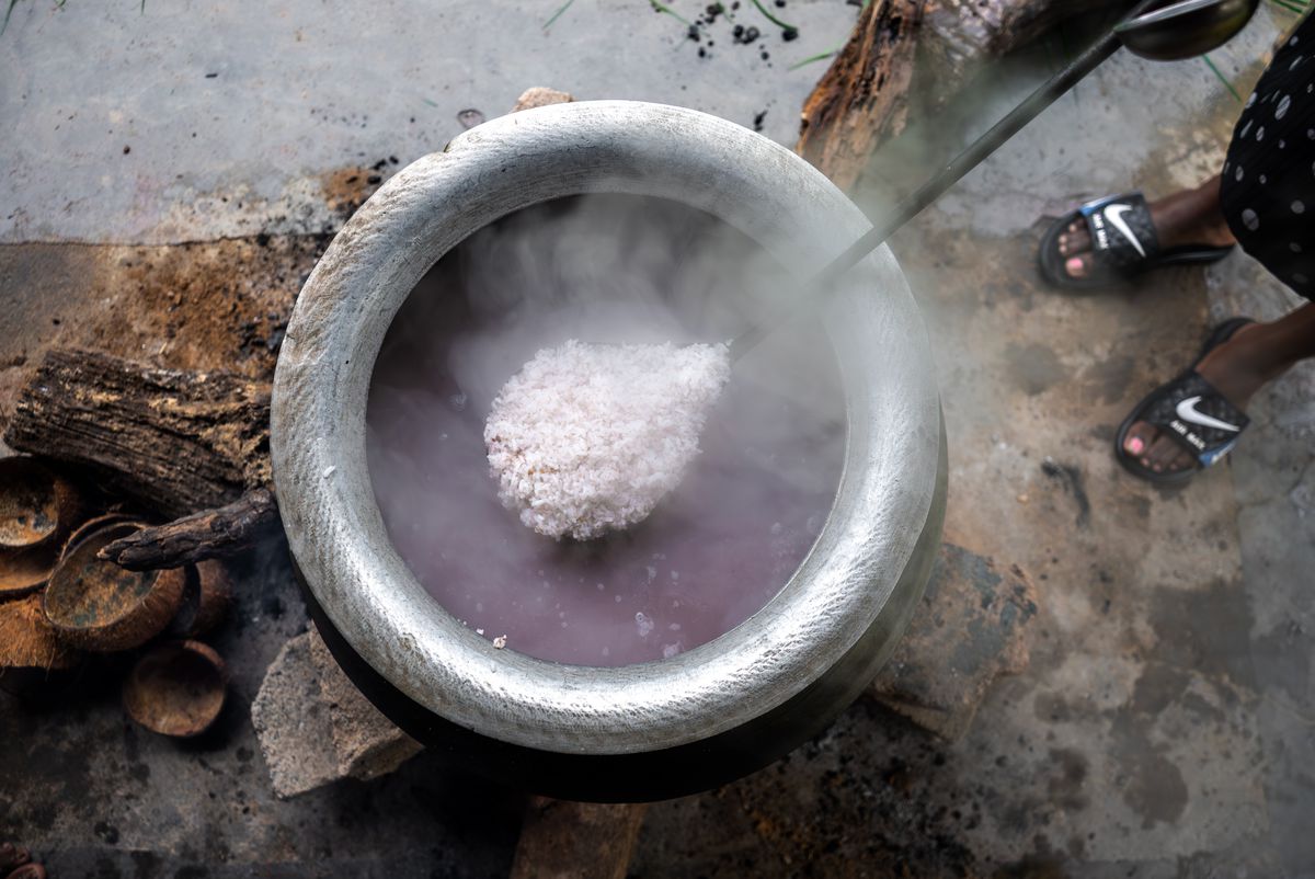 A large pot of shot from above. A large spoon holding a pile of rice is held aloft above the greyish, purplish liquid.