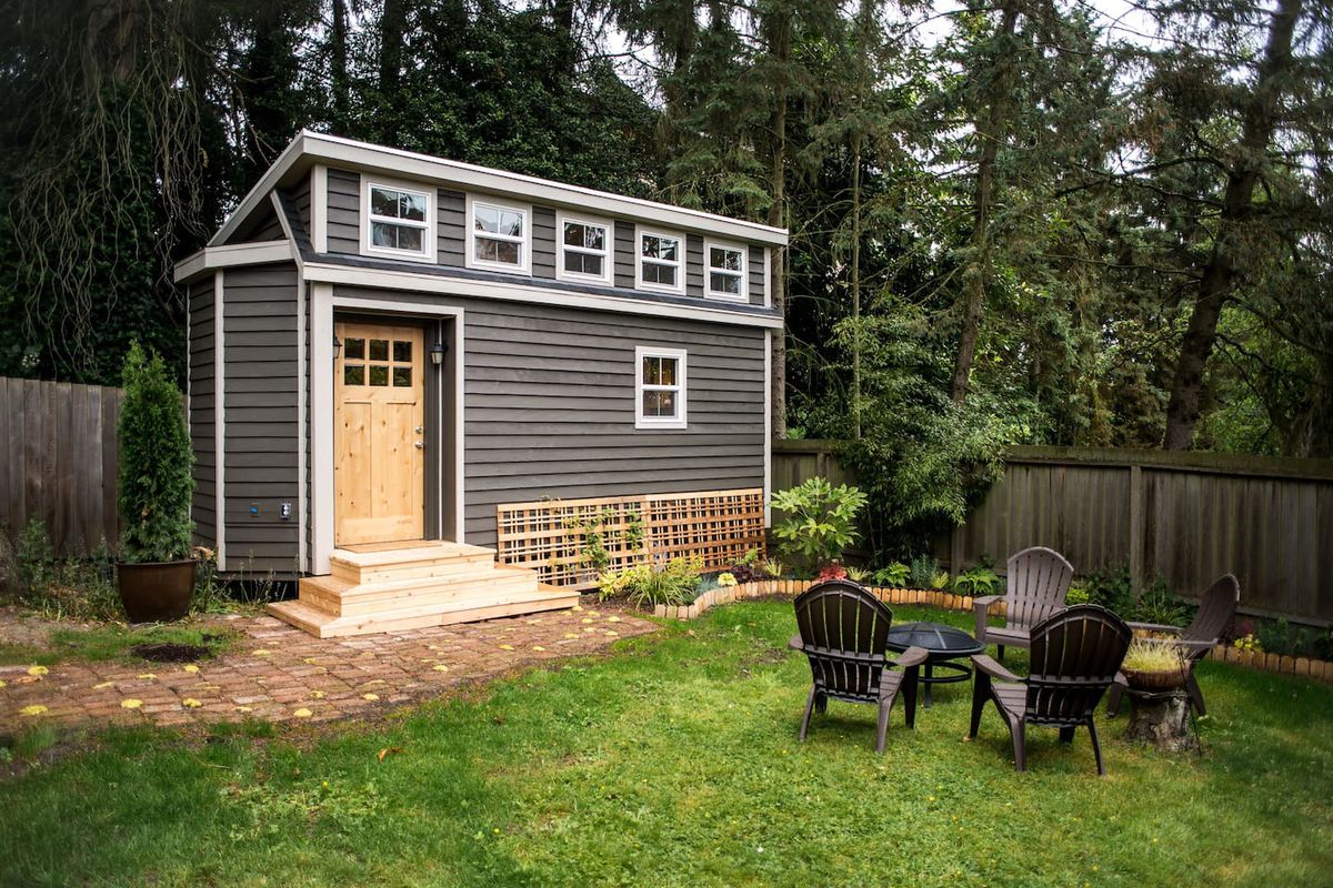 The backyard of a tiny home in Seattle. There is grass, a table and chairs. The house has a gray exterior with a wooden door.