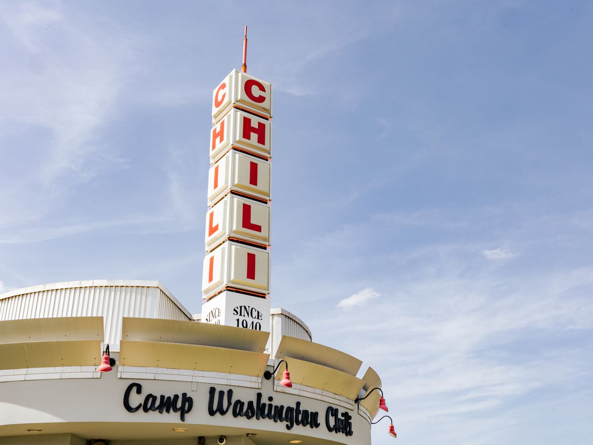 The sign on top of a restaurant exterior, with the word ‘chili’ extending upward in red letters above ‘Camp Washington Chili’.