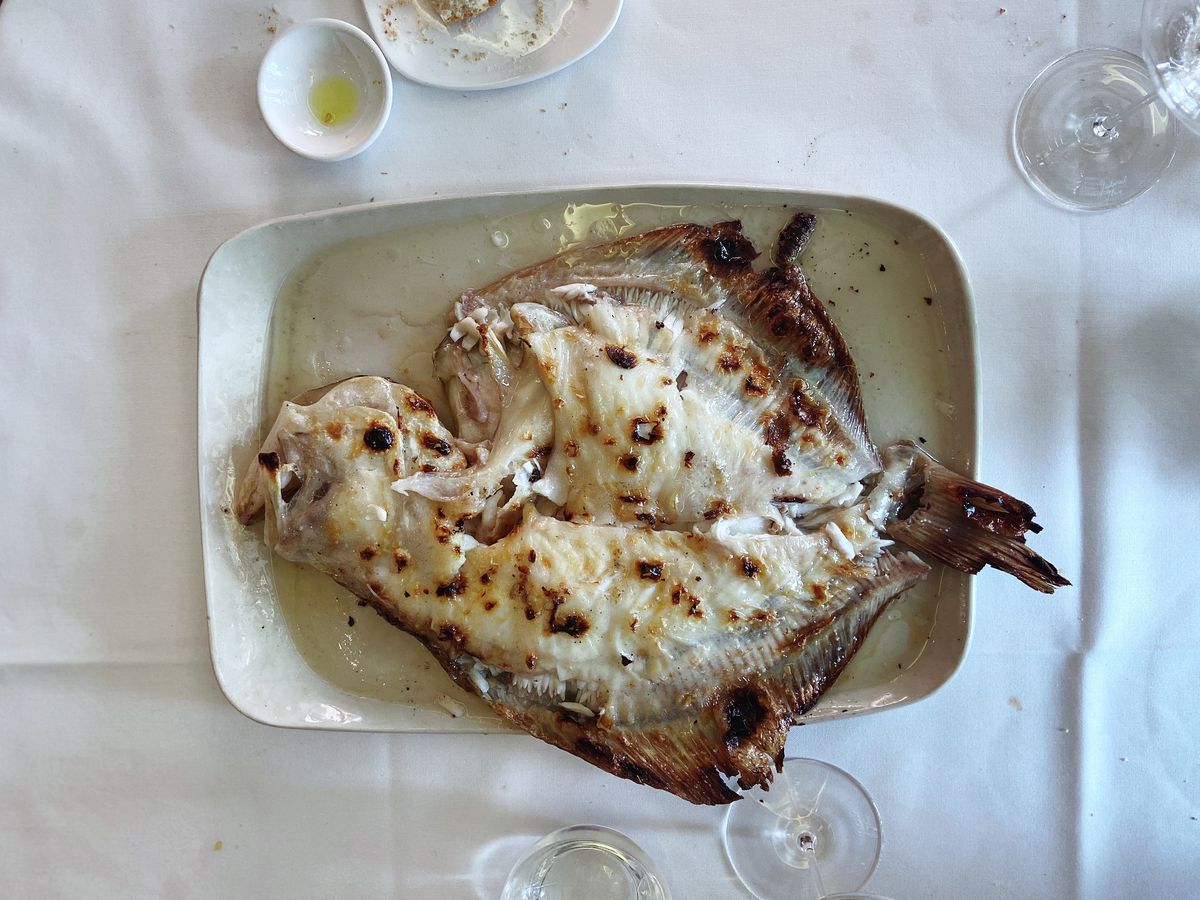 A whole grilled fish on a plate on a white tablecloth