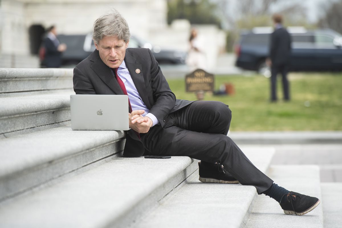Representative Tom Malinowski, sitting on the steps of the House while looking at a laptop.