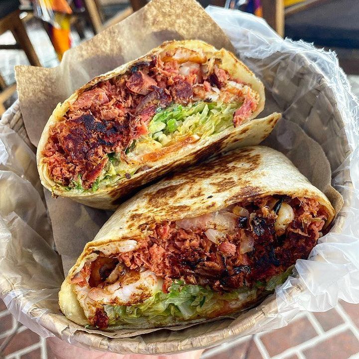 A burrito stuffed with a deep red chopped seafood mixture, guacamole, and other ingredients, sliced in half to reveal the interior. 