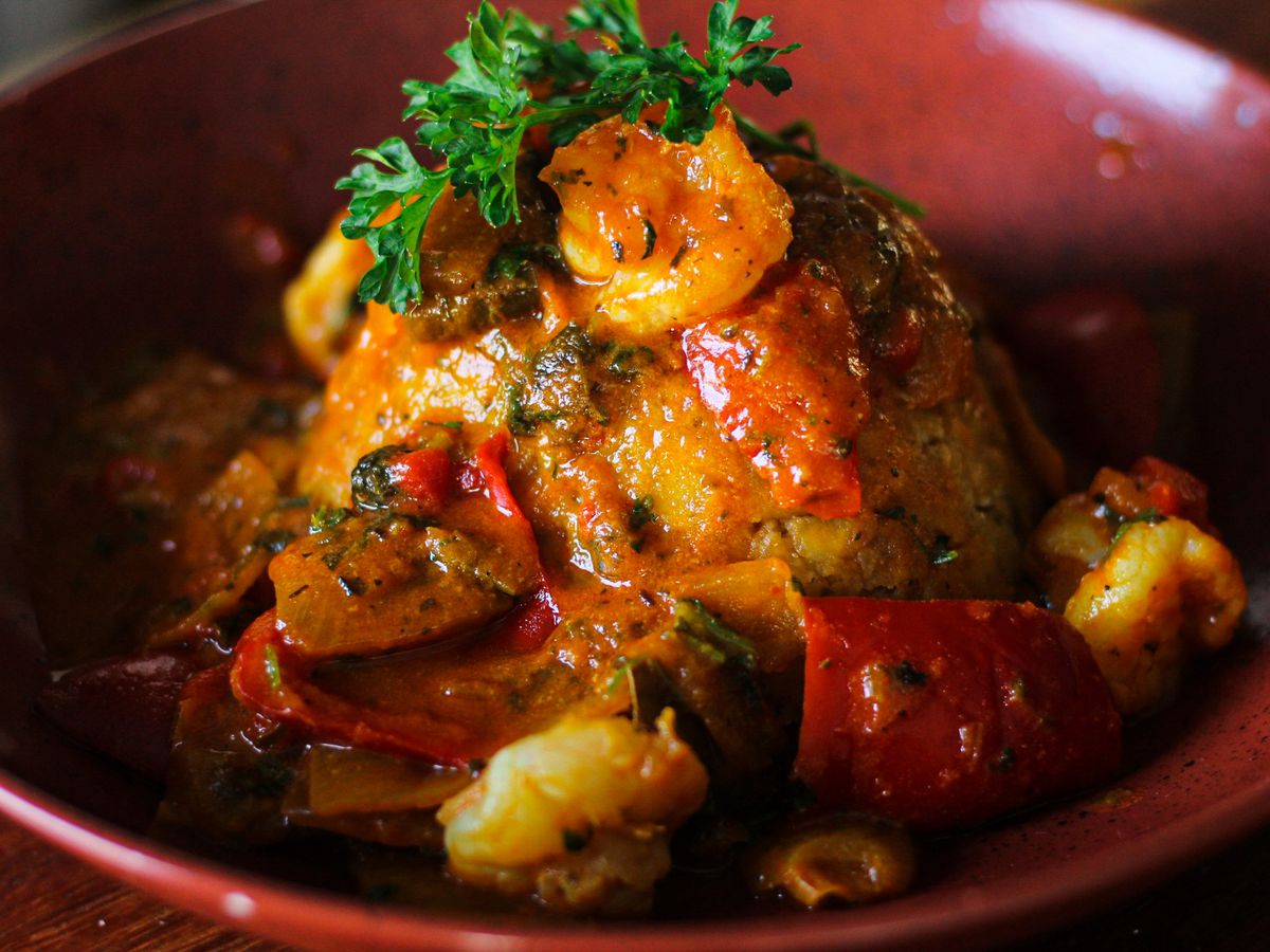 A sauce covered mofongo with shrimp, tomatoes, and cilantro in a deep dish.