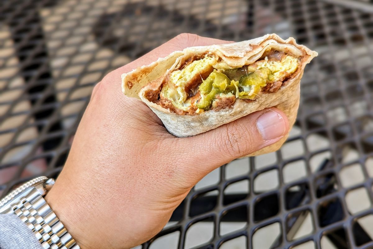 Bitten burrito with green chile held by a hand.
