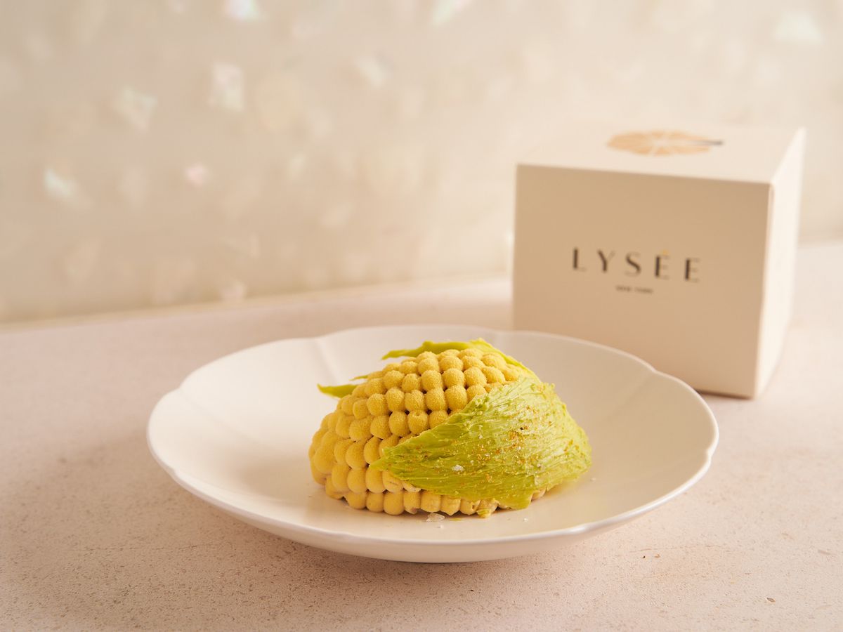 A white bowl holds a round dessert that looks like corn on the cob. In the background a box that says Lysee stands.