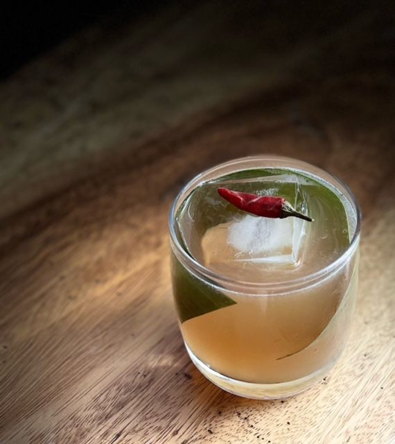 A lowball cocktail with a bamboo leaf and dried chili pepper.