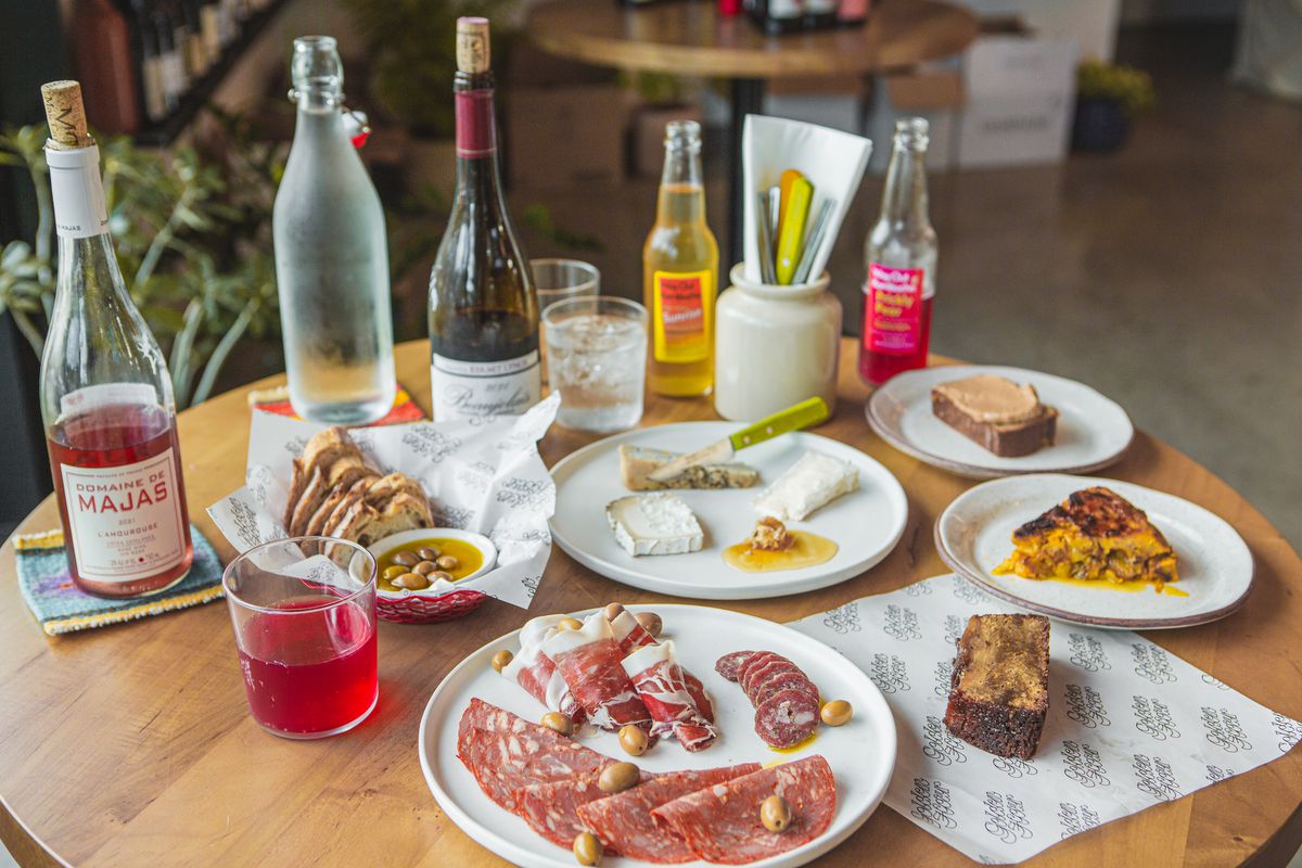 A stable set with plates of food including sliced meats, and bottles of wine.