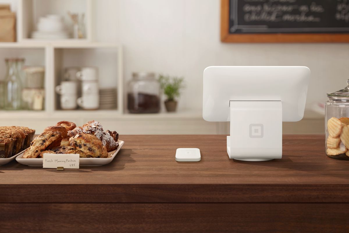 A white Square stand and contactless card reader sits on a cafe counter with pastries.