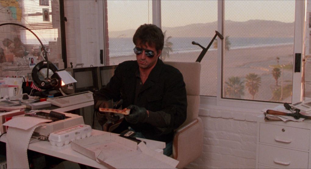 Sylvester Stallone, wearing sunglasses, cuts a slice of pizza with a pair of scissors in Cobra.