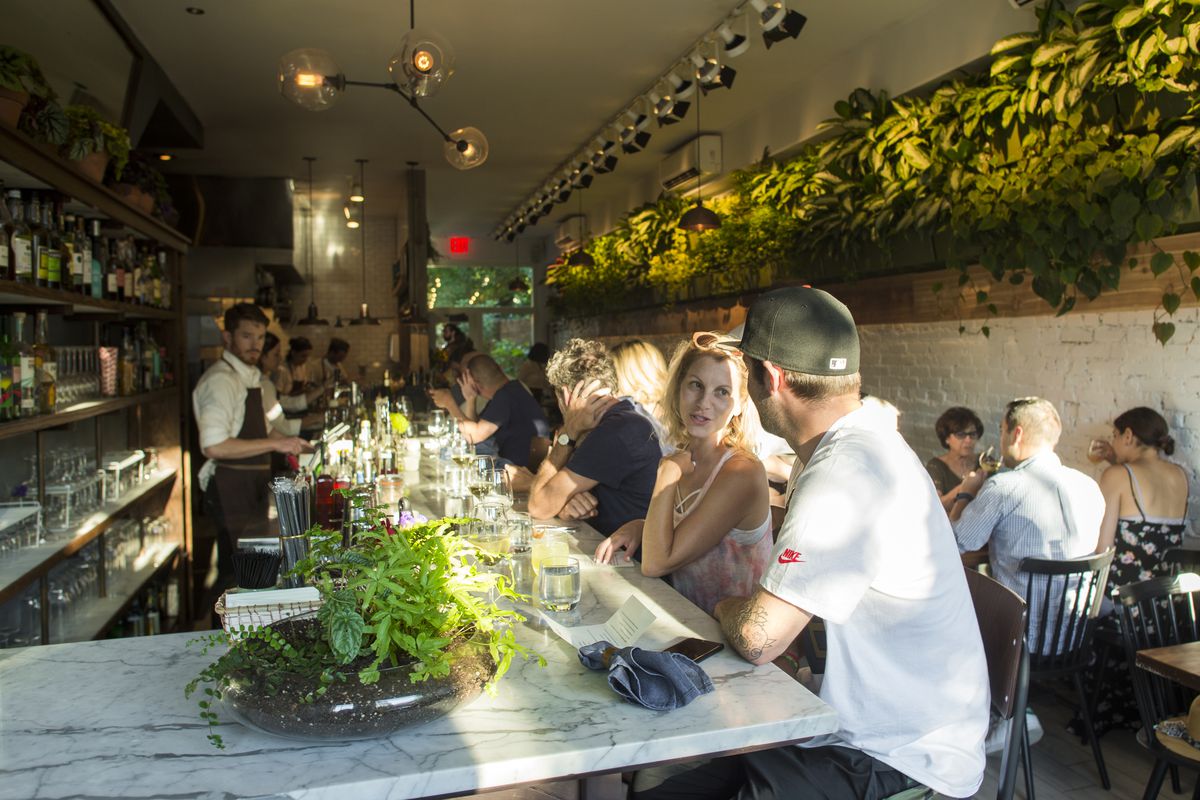 Patrons sit at the bar at Olmsted surrounded by plants