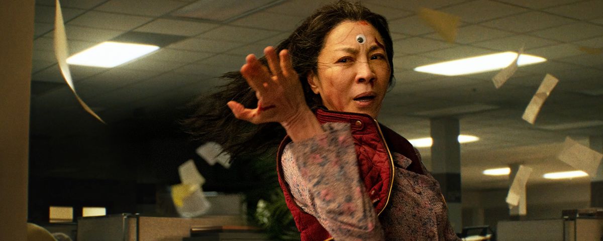 A bloodied Michelle Yeoh with a googly eye pasted on her forehead strikes a martial-arts pose in Everything Everywhere All at Once