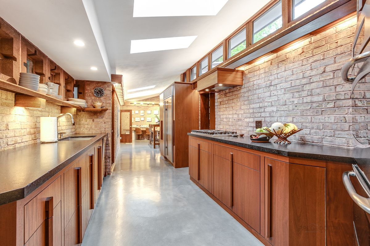 A long, narrow kitchen has slate kitchen counters, concrete floors, and wood cabinets.