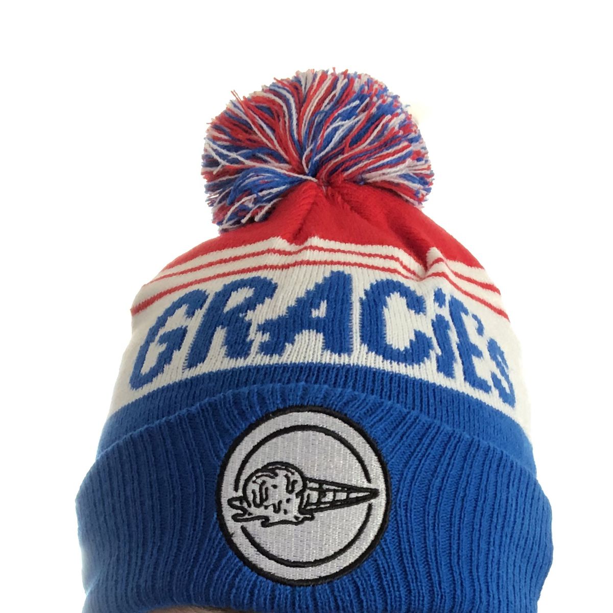 A winter hat with a pom pom in red, white, and blue. Text reads “Gracie’s,” and there’s an image of a melting ice cream cone on a patch on the front.