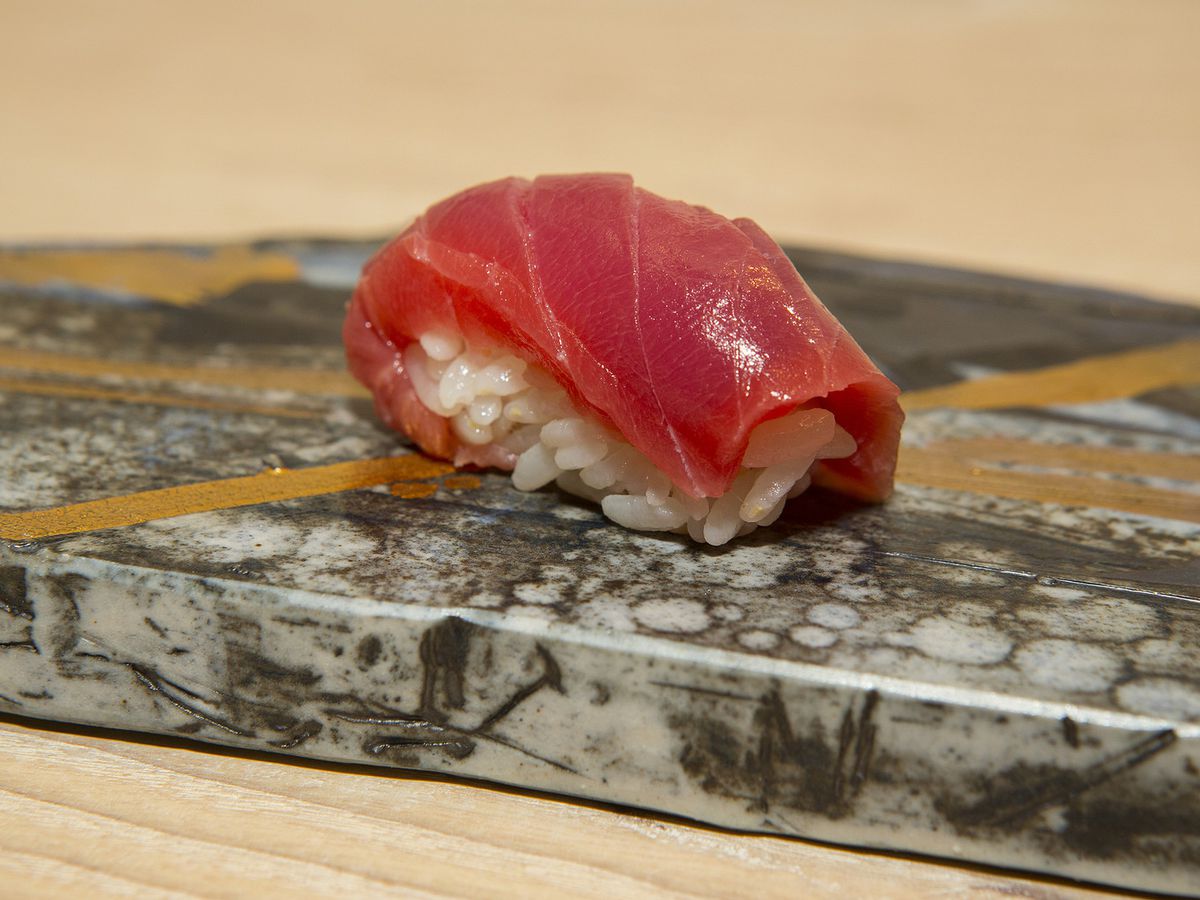 A piece of nigiri with a slice of raw, red fish on a bed of white rice.