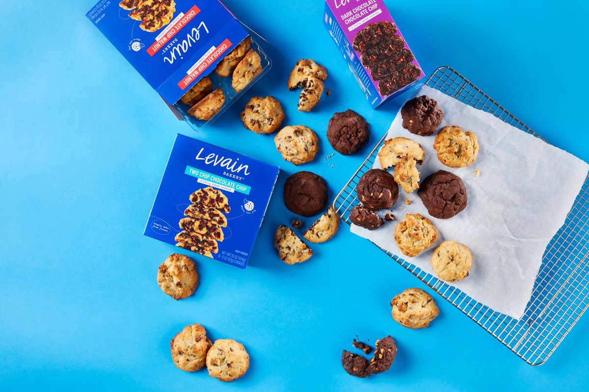 An overhead shot of three types of cookies spilling out from boxes marked “Levain” on a blue background