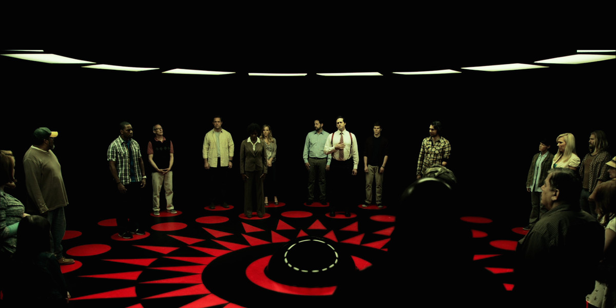 Contestants from 2015’s Circle stand in the death machine, a circular black room with space-age lighting in the ceiling and a red geometric pattern in the floor.