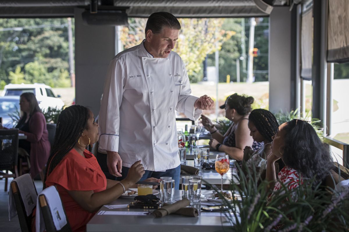 At the 2021 Atlanta Food and Wine Festival brunch event, Chef John Metz of Woodall in Atlanta talks to two women sitting at a table in his restaurant. 