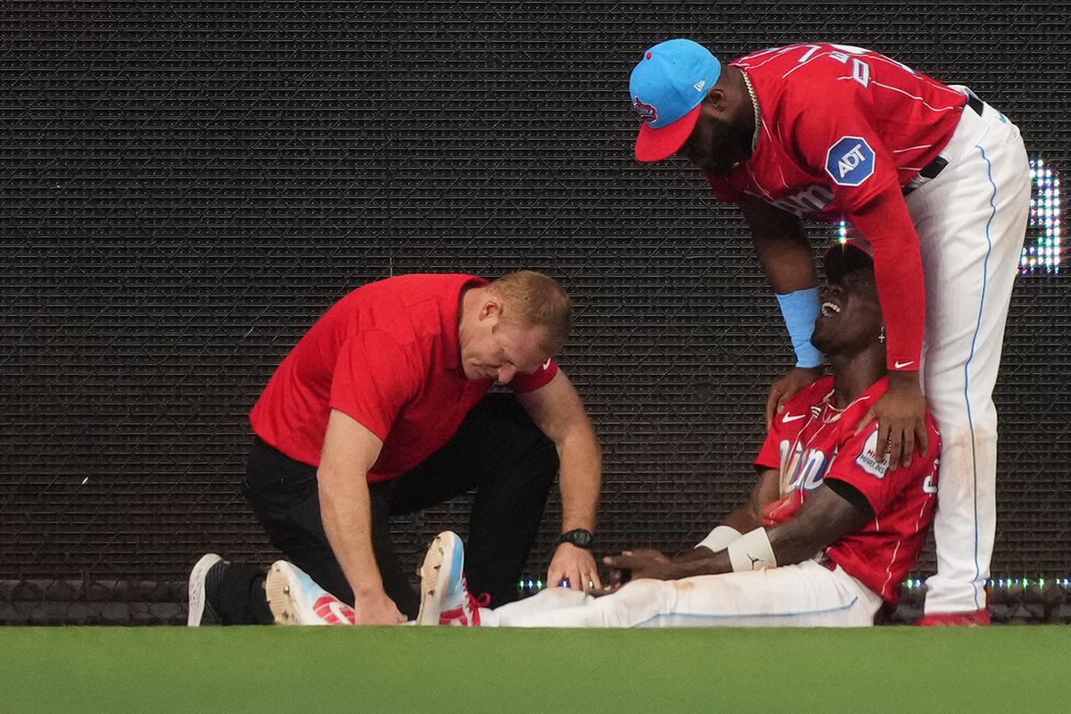 Jazz Chisholm Jr. #2 of the Miami Marlins is attended to by a team trainer and Bryan De La Cruz #14 after an apperant injury in the game against the Cincinnati Reds at loanDepot park on May 13, 2023 in Miami, Florida.
