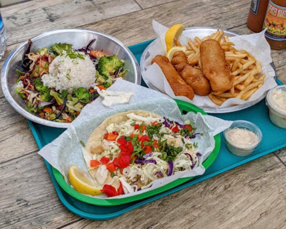 A wooden table holding a tray of fried seafood, a taco, and salads.