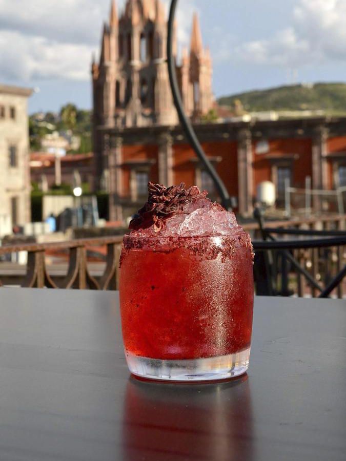 A red drink in a glass on a table with a view of a cathedral in the background. 