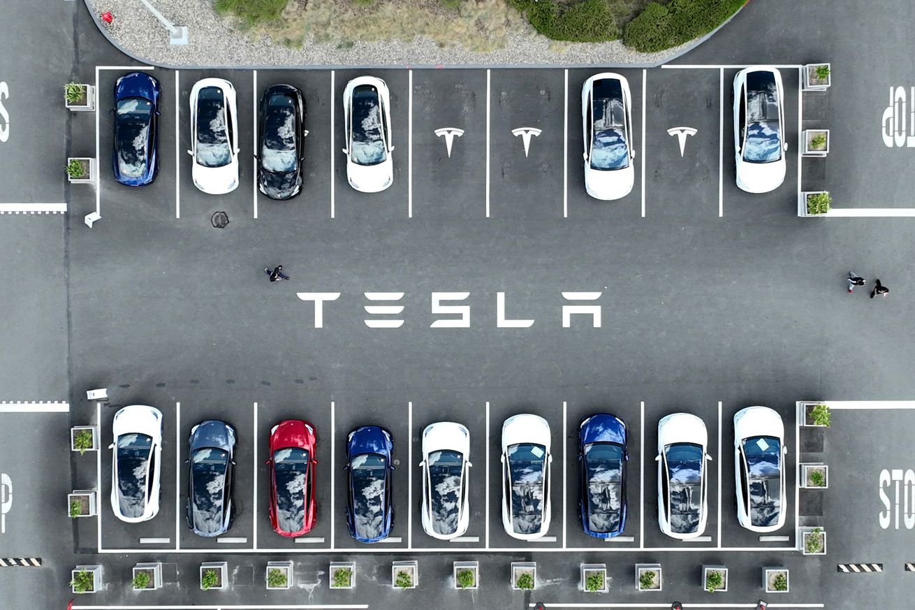 Two rows of Tesla cars in a parking lot, photographed from above.