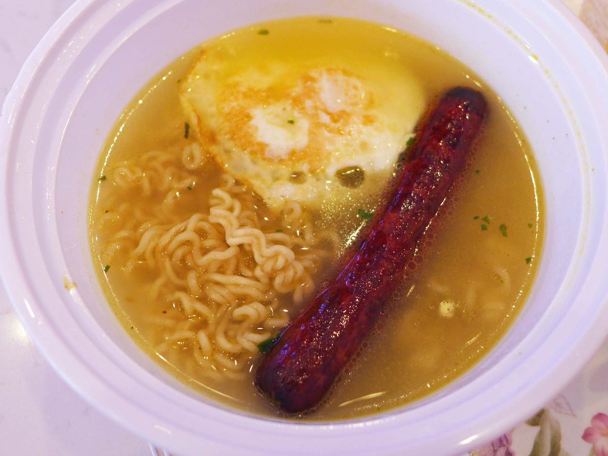 A hot dog, fried egg, and wavy noodles in a yellowish broth.
