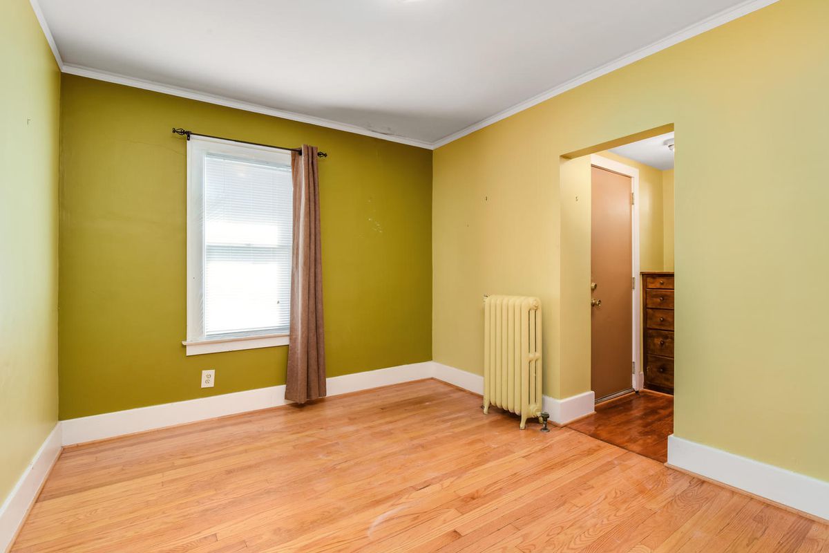 An empty room with yellow-green walls and hardwood floors.