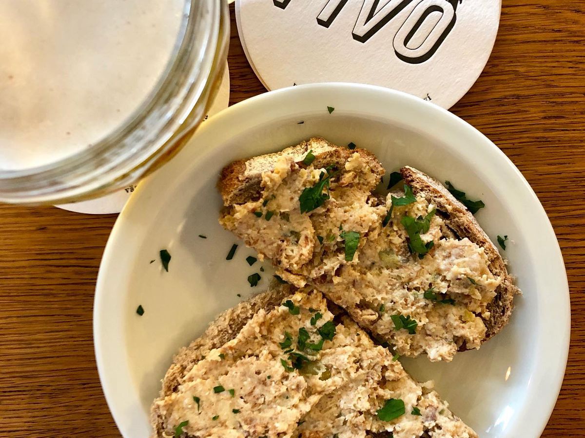 From above, two slices of toast topped with ground pork spread and garnishes, next to a full glass of beer and a coaster bearing the name Pivo 