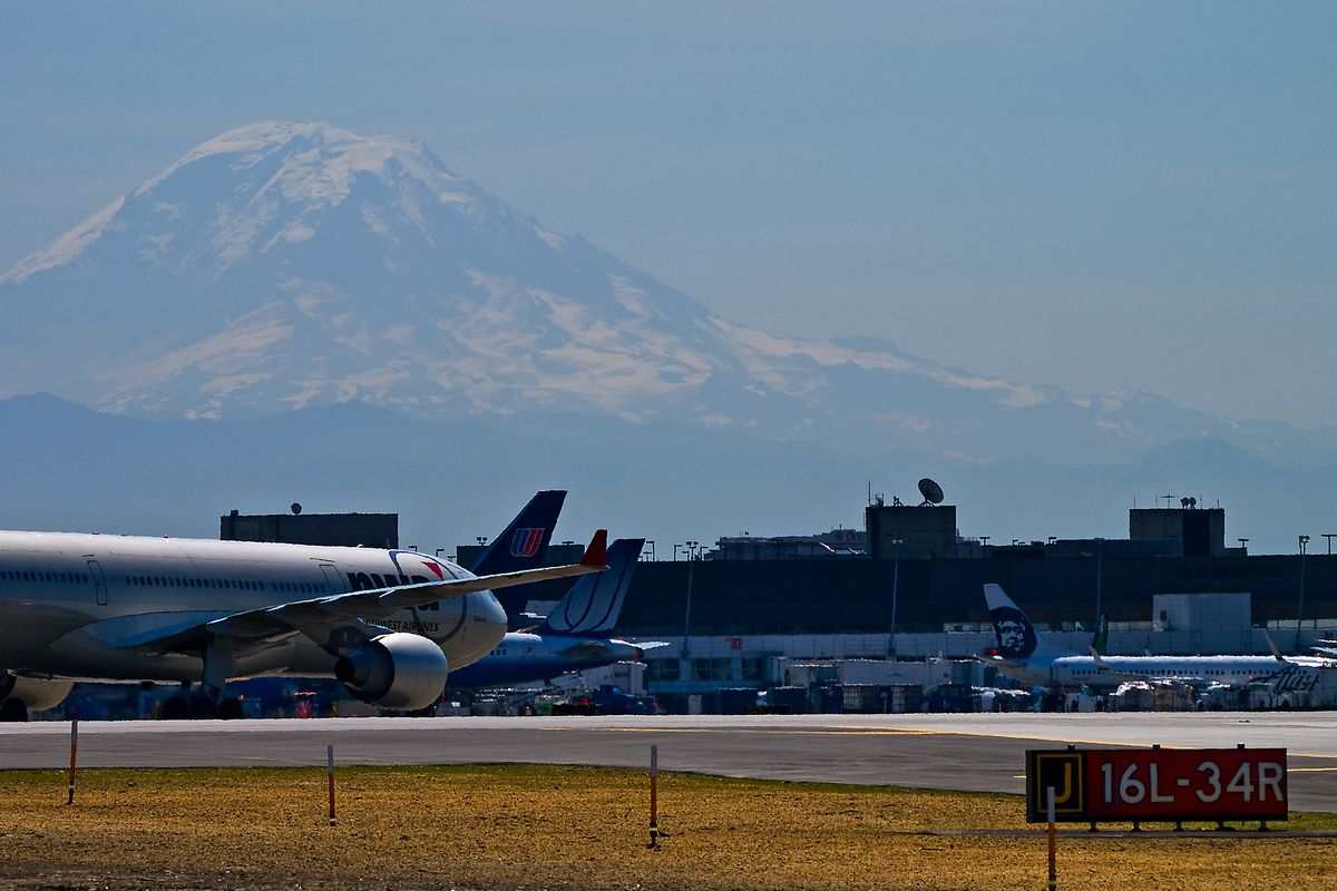 Seattle-Tacoma International Airport with an airplane on a runway in the foreground and Mt. Rainier in the background.