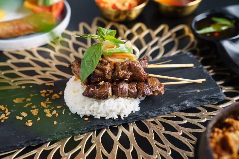Skewers of cooked beef sit on a pile of white rice garnished with herbs and other vegetables.