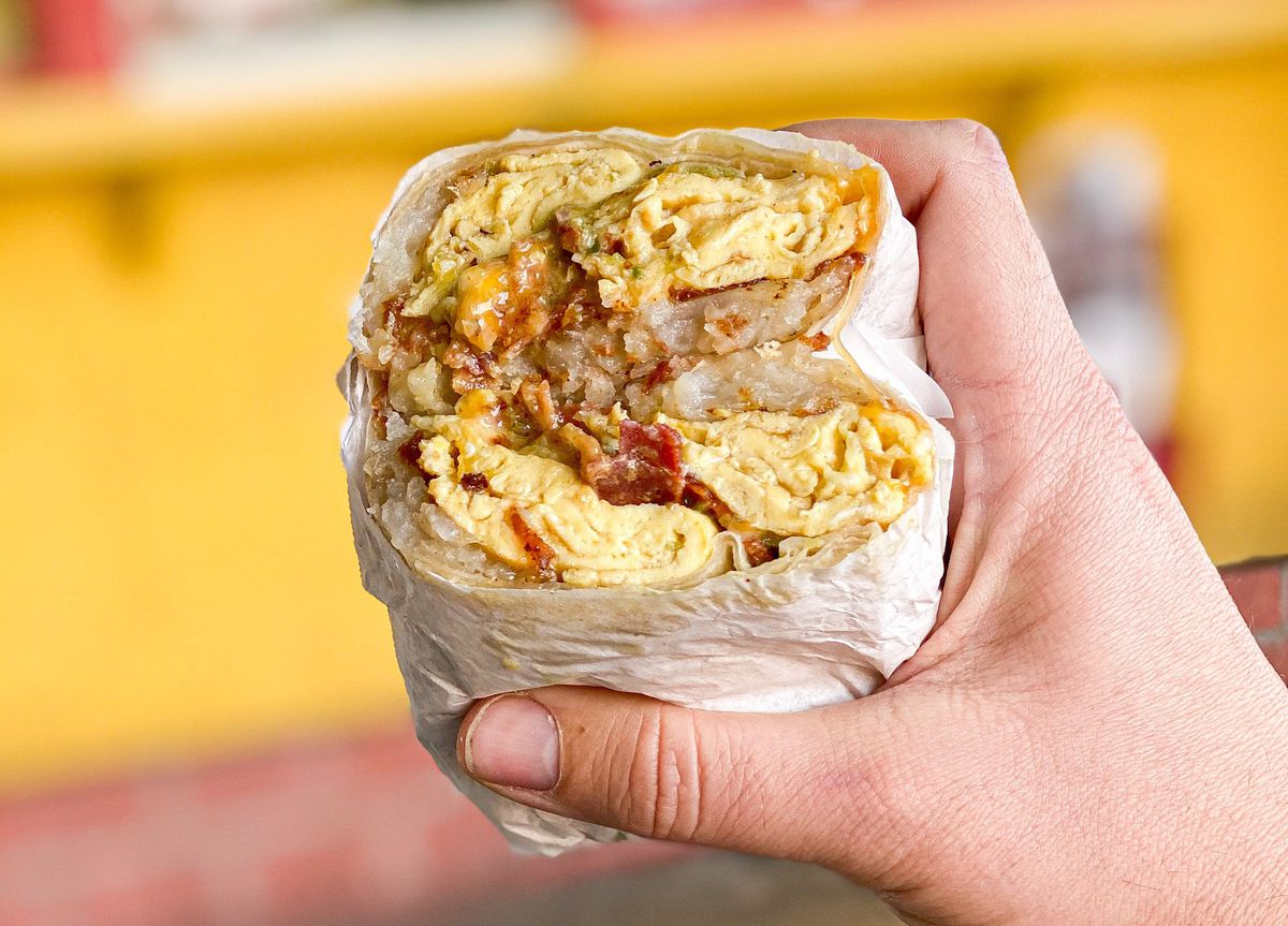 Larry’s Chili Dog breakfast burrito held in a hand with a yellow background.