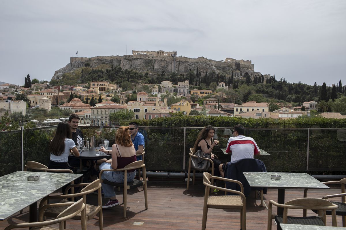 People sit in on a cafe terrace, in the Monastiraki district of Athens, with the ancient Acropolis hill in the background, Monday, May 3, 2021.