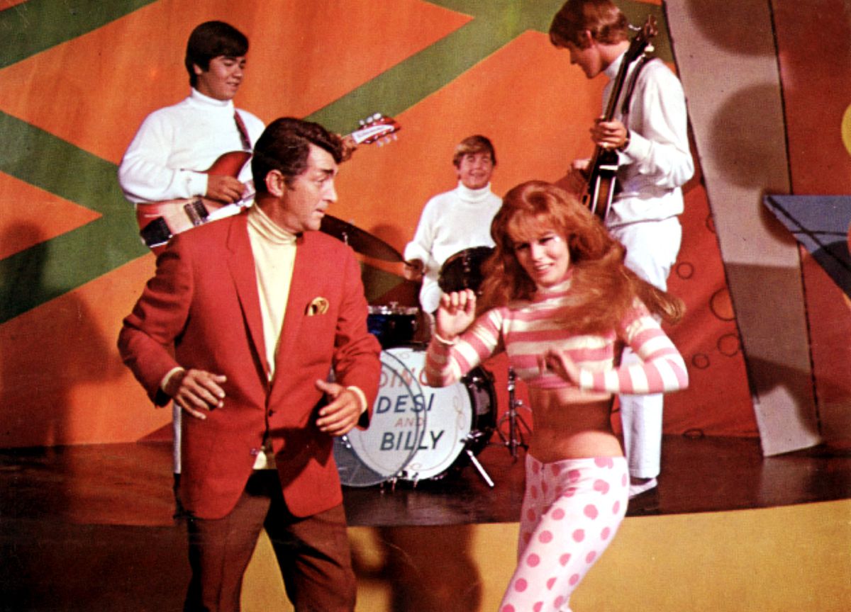 Matt Helm in a red suit dances with a redheaded girl in front of the band Desi and Billy