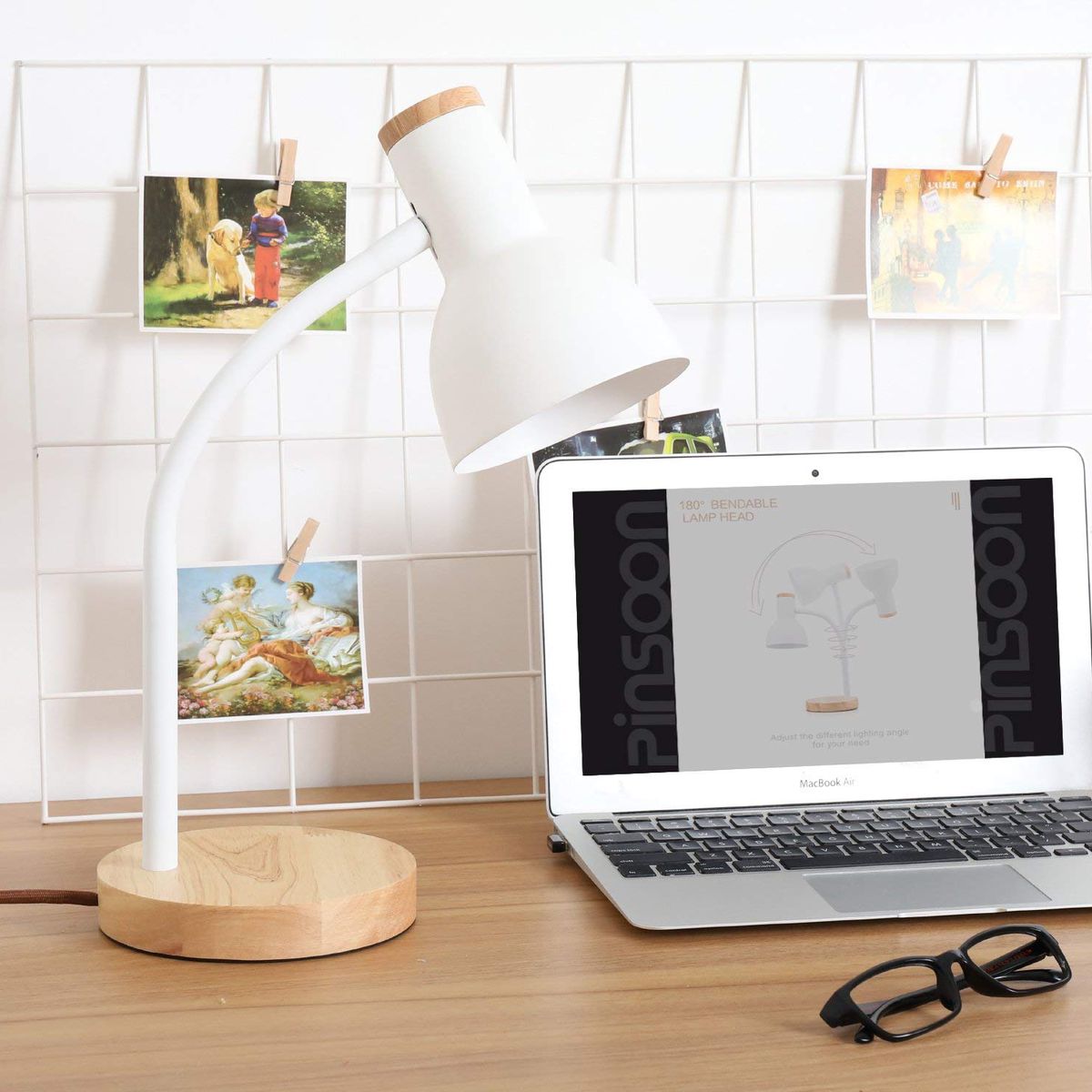 A small white and birch wood desk lamp sits next to a laptop computer. A wire photo display sits behind the lamp. 
