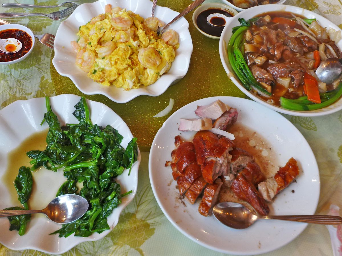 Several plates of Chinese food including shrimp with scrambled eggs, roast duck, and steamed greens.
