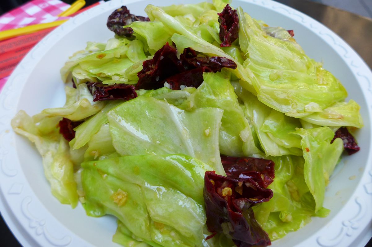 Green sauteed napa cabbage with dark red dried chilies spilling seeds.