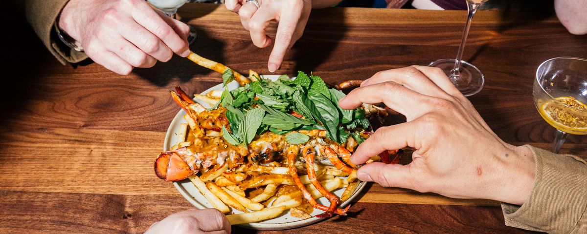 Hands dive in to pick up fries on a plate with a whole lobster on it.