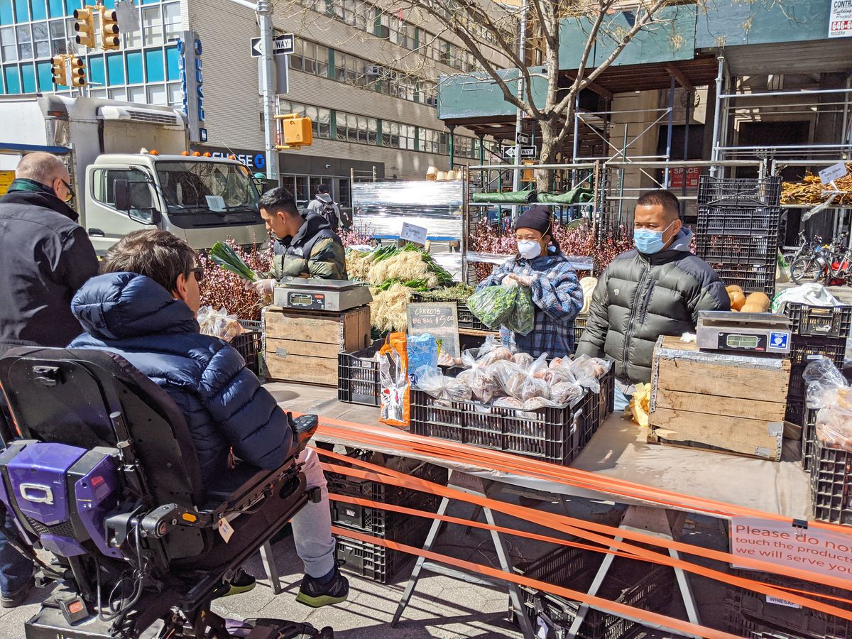 A man in a motorized wheelchair contemplates the plastic  bags of spinach.