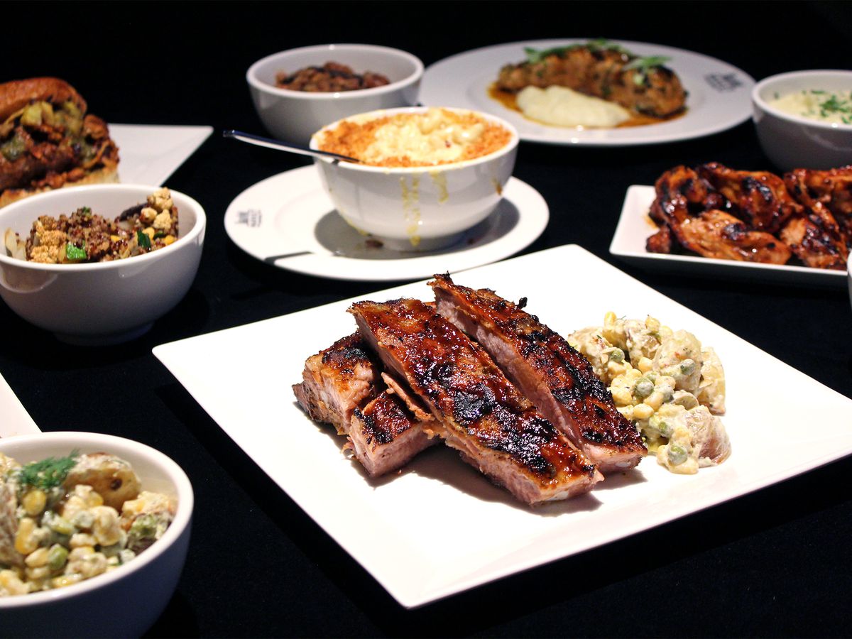 an array of barbecue meats on white plates against black background