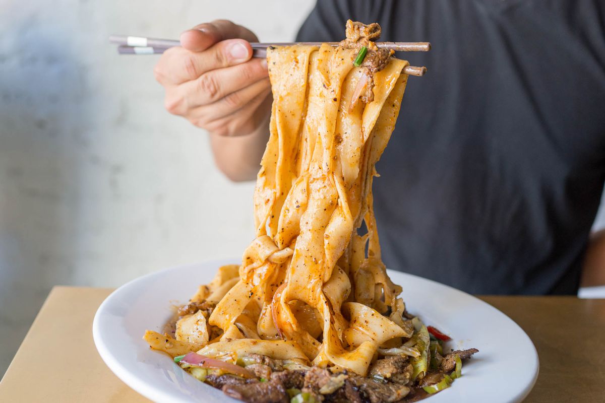 Xi’an Famous Foods’ spicy cumin lamb noodles sit on a white plate as a person pulls them up
