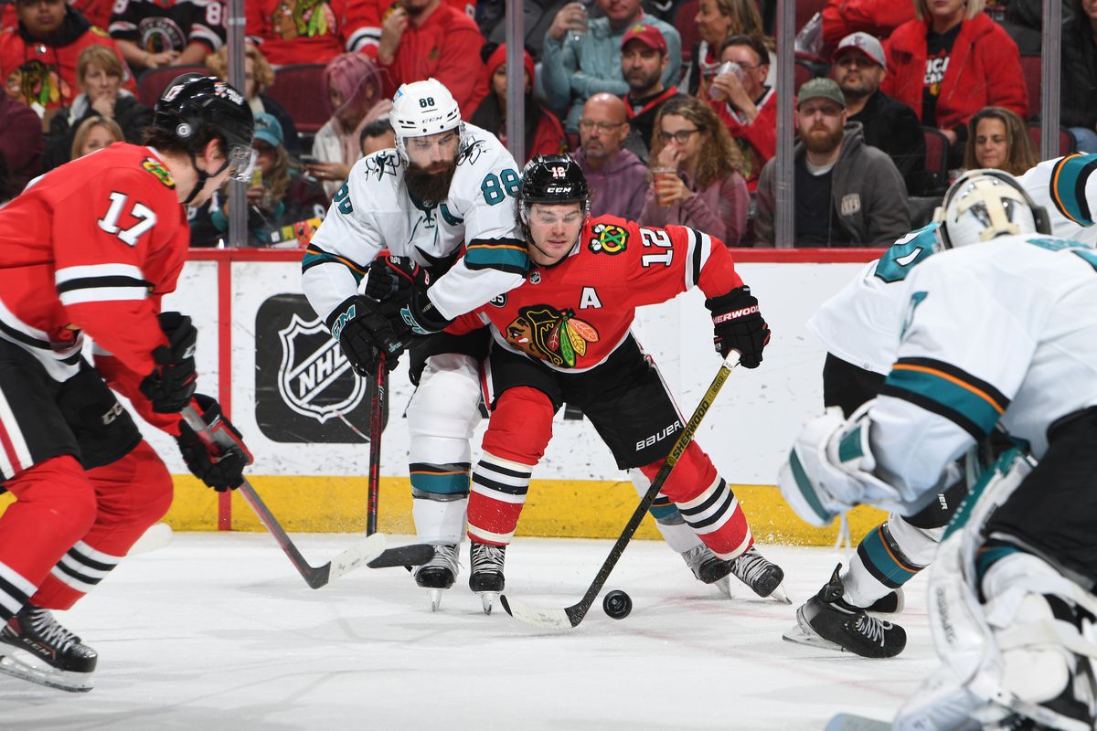 Brent Burns #88 of the San Jose Sharks and Alex DeBrincat #12 of the Chicago Blackhawks battle for the puck in the third period at United Center on April 14, 2022 in Chicago, Illinois.
