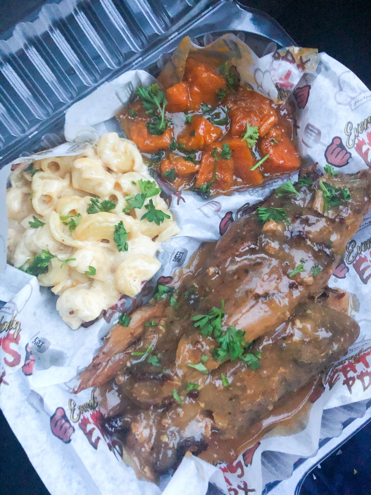 A takeout container of mac and cheese, yams, and turkey legs arrives with a sprinkle of parsley at Everybody Eats