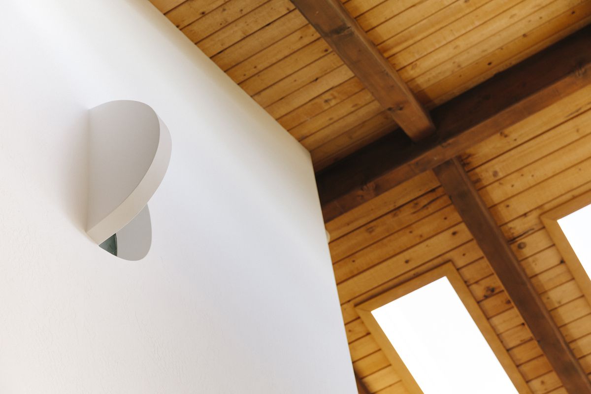 A view looking up in the corner of a room. There is a wooden ceiling and two skylights. The wall is painted white. 