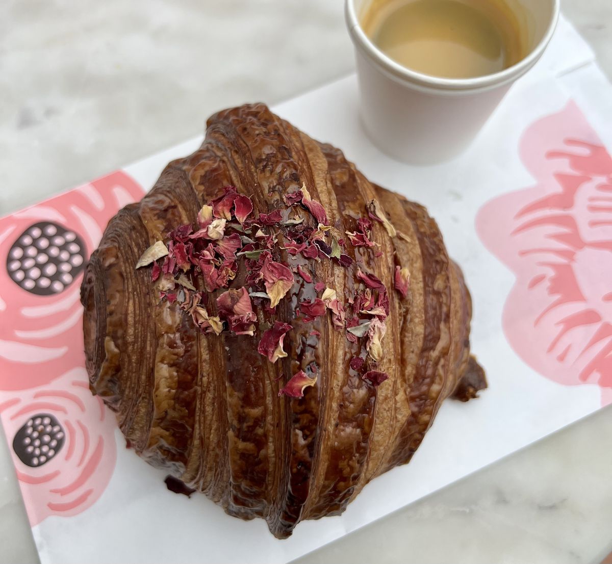 A croissant topped with dried rose petals on a rose patterned plate at Artelice Patisserie.