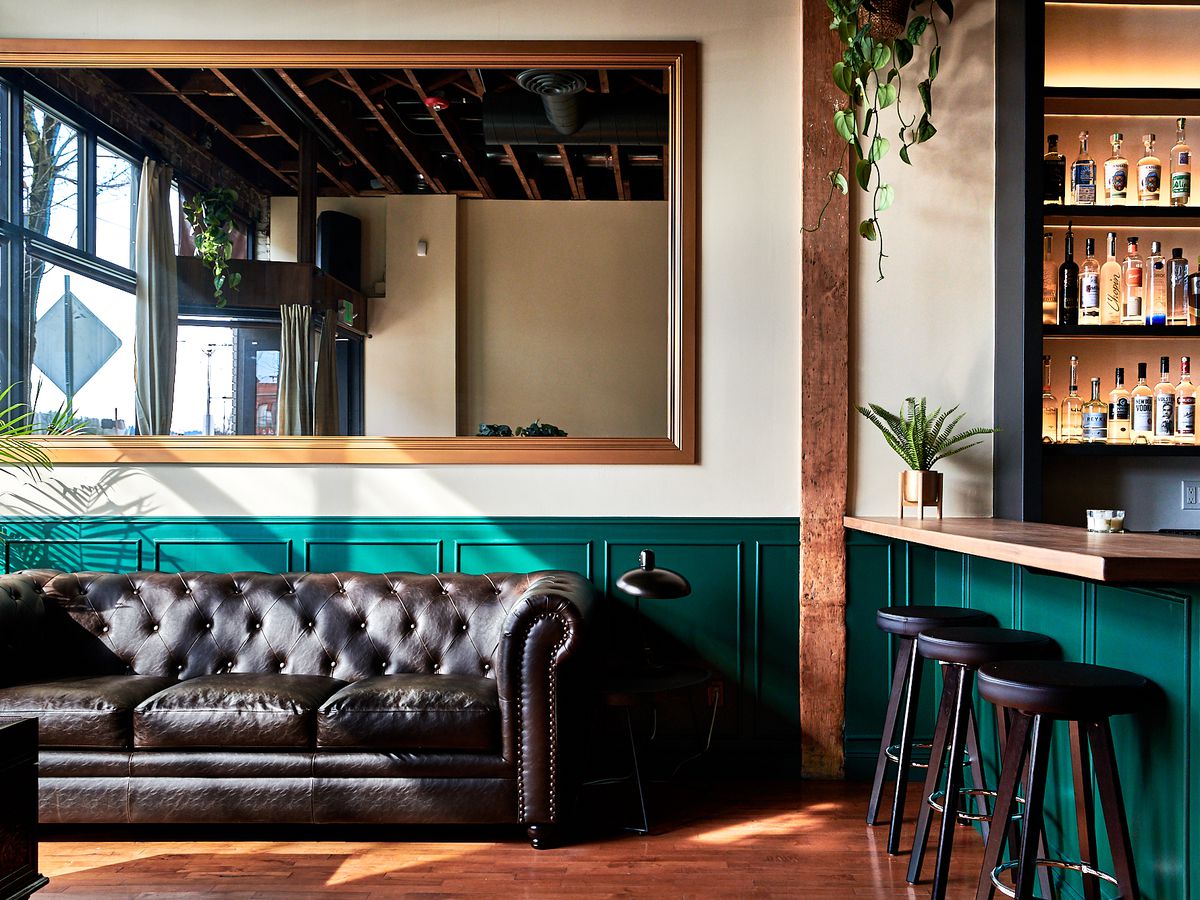 A black couch sits under a large mirror at Lulu, with teal backsplash below white walls