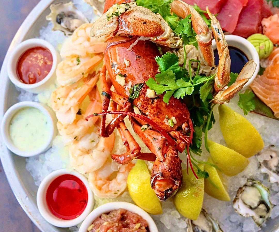 A whole lobster on ice with lemon and sauces.
