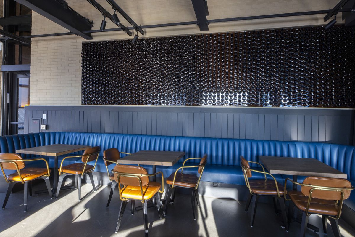 A dining room with a long blue banquette and wall art installation made from hundreds of blue bottles. 