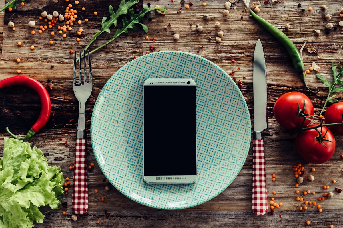 A cell phone on a white plate with a knife and fork on either side.
